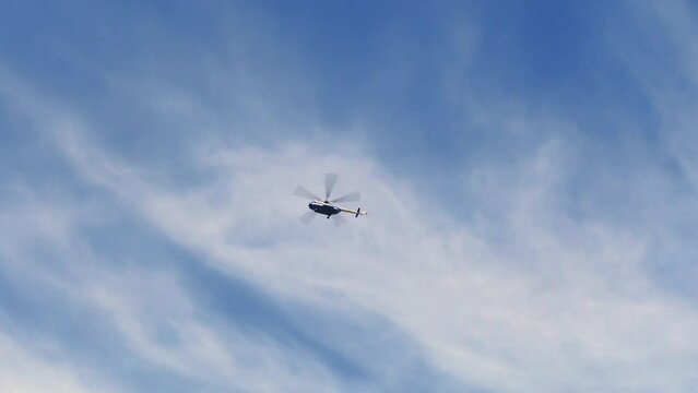 Bottom View Of High Flying Transport Helicopter Blades Spinning Fast. Silhouette Chopper Flies Quickly Across Blue Sky With Clouds. Aviation In Hard-to-reach Places. Military Helicopter Flies Airfield