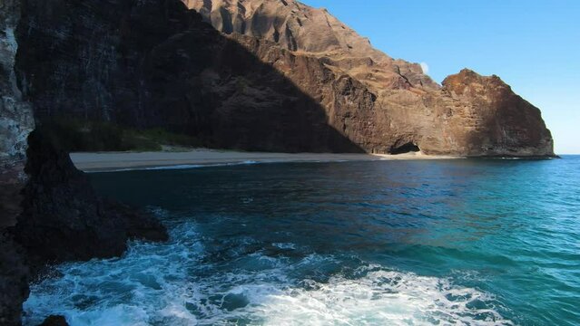 Flying above the ocean waves towards the sandy beach of Na pali coast, Kauai, Hawaii