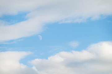 Peaceful blue sky with white clouds and a half moon, as a nature background
