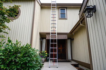 Fototapeta na wymiar Getting ready for fall home maintenance, tall aluminum extension ladder against a two-story house 