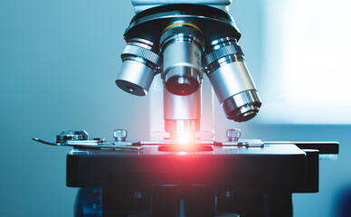 close up of compound microscope with ray of orange light shining in lab setting