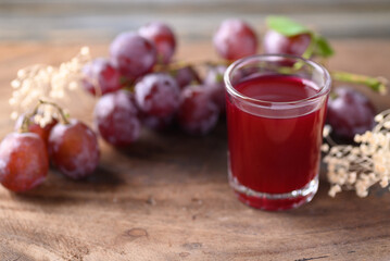 Red grape and juice in glass on wooden background