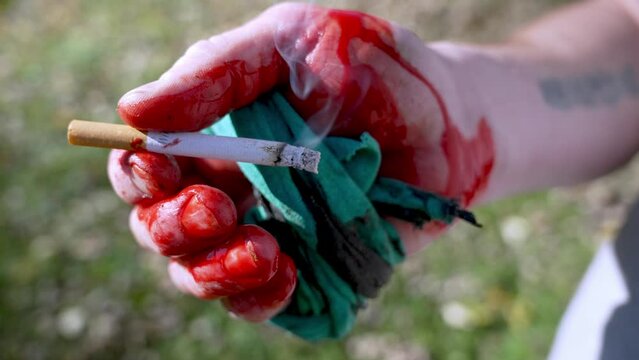 Close up Bleeding hand with Fabric tourniquet holding a lit cigarette, Conceptual