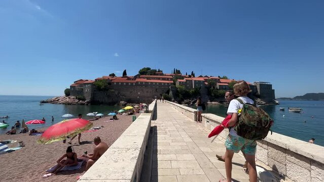 The Sveti Stefan entrance bridge, still tripod shot of a family of tourists and a dog walking down the stone bridge to see the lovely and expensive hotel in Montenegro filled with celebrities.
