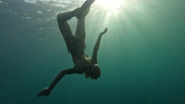 Fabulous blonde woman swimming underwater towards the ocean surface lit by the sun rays