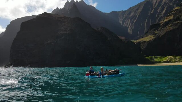 Romantic couple relaxing on a canoe in the water of the Pacific Ocean near the coast of Na Pali, Kauai, Hawaii