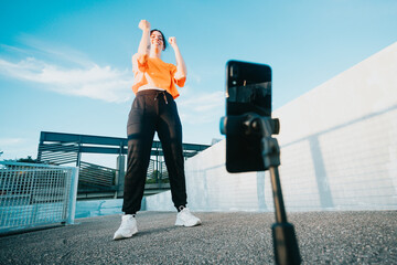 Young woman on urban clothes recording a video dancing while streaming it for the followers on phone