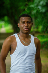 Chico afro latino viendo al frente usando un camiseta blanca con fondo verde y boscoso