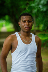 Chico afro latino viendo al frente usando una camiseta blanca con fondo verde y boscoso