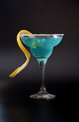 Tall glass with blue curacao liqueur with ice and lemon zest on a black background.