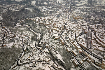 Fototapeta premium Aerial winter landscape of dense historic center of Thiers town in Puy-de-Dome department, Auvergne-Rhone-Alpes region in France. Rooftops of old buildings and narrow streets at snowfall