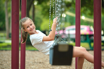 Young pretty smiling teenage girl playing alone on swings on summer playground