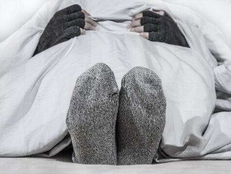 Eine Person liegt im Bett und wärmt sich mit dicken Socken und Handschuhen