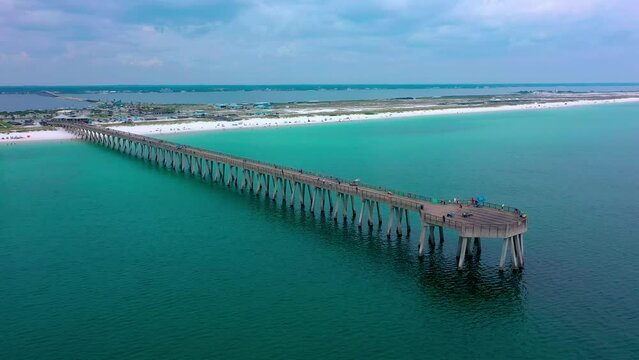Aerial drone panning right view of the Navarre Beach Florida Pier with some dark clouds and the white sand beach in the background.