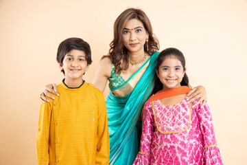 Portrait of Indian mother with kids wearing traditional cloths as they celebrate diwali standing isolated on studio background, Festival or auspicious occasion,