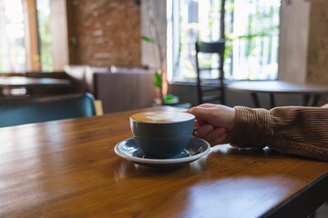 Closeup image of a hand holding coffee cup on wooden table