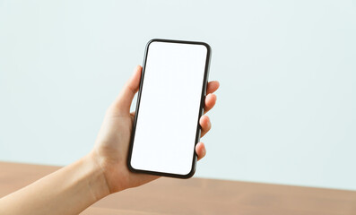 Hands holding smartphone with mockup of blank screen on sofa in living room.