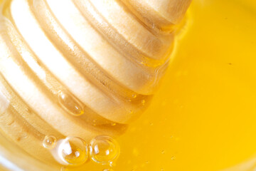 Honey drips from a wooden honey dipper on a yellow background. Sweet bee product for your design...