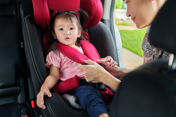 mother is fastening safety belt to toddler girl in car seat