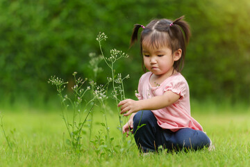 toddler girl sitting and playing grass flower in field