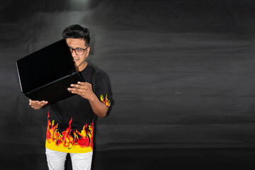 Man in glasses and polo shirt with flames holds a laptop. Technology concept on black gradient...