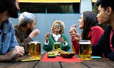 Multiracial friends enjoy some beer and laughing together in outdoors bar.