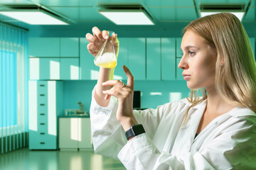 Young woman nurse. Girl with medical test tube. Yellow liquid in glass flask. Woman nurse in white coat. Medical student. Girl examines flask while standing in hospital. Nurse portrait at working