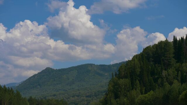 This stock video shows beautiful nature - mountains overgrown with trees, white clouds in a blue sky. This video will decorate your projects related to nature, travel, tourism, mountains.