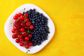 berries of cherries and blueberries on a plate, summer seasonal berries, on a yellow wooden background