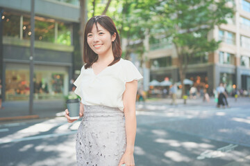 Fototapeta premium オフィス街でコーヒーを飲みながら歩く女性