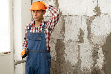 Thoughtful young builder with a spatula on the background of a wall of white bricks, making a wall...