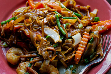 Drunken noodles, pad kee mao, with prawns, basil, chilii, peppers and green beans. Close-up on a plate.