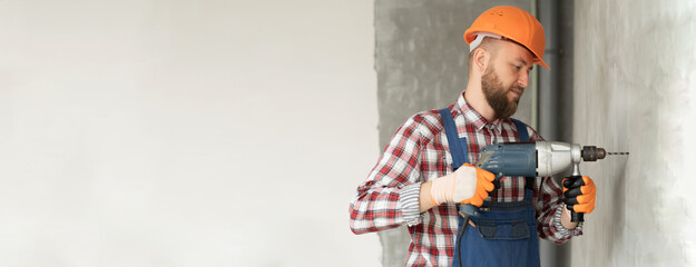 Laborer man in protective gloves drills concrete wall with drill. Repair service and construction concept. Banner