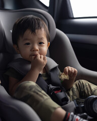 Happy Asian Chinese age 1-2 years old kid enjoying his food while sitting on safety car seat
