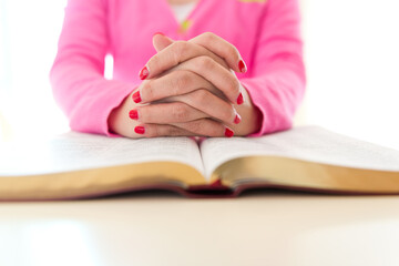 Young woman faithfully prays with her hands on bible.