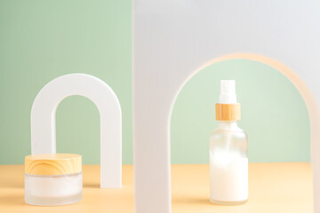 Mock up glass dropper bottle and face cream jar on a white podium on a beige background with soft shadows. Skin care products in trendy presentation