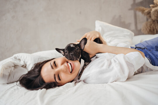 happy Beautiful brunette woman with a French Bulldog puppy in a bed.