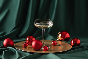 Merry Christmas and Happy New Year. Glass of champagne with red Christmas ornaments over green...