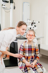 ophthalmologist picks up glasses for a little girl at an appointment in a clinic