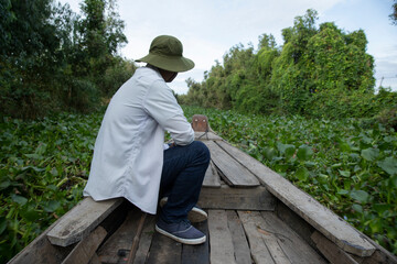 Early morning boat ride along a canal in the Mekong delta, Vietnam. A male worker is sitting on the...