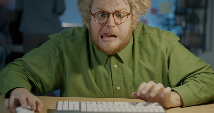 Portrait of emotional young man typing with computer keyboard then showing thumbs-up in dark office at night. Technology and business success concept.