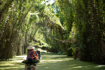 A group of tourists and local guide paddle a canoe along a beautiful canal with overhanging trees...