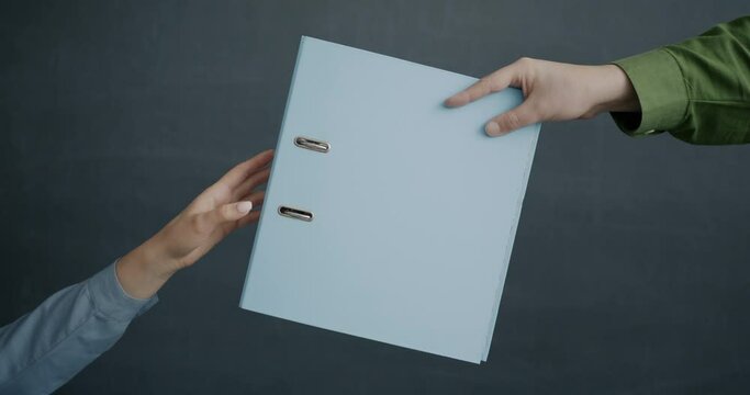 Close-up of human hands male and female holding and giving paper folder on gray background. Office supplies and business stationery concept.