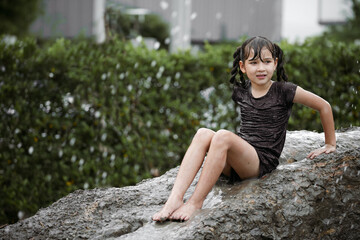 Cheerful child girl playing on heap of wet soil during raining in rainy season.