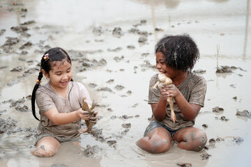 Two happy children child girl catching big frog in the large wet mud puddle on summer day.