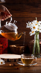 A teapot and a mug of tea on a wooden table and a bouquet of daisies