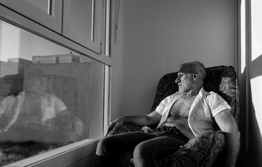 Monochrome of adult man sitting on chair against window with sunlight and shadow