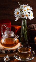 A teapot and a mug of tea on a wooden table and a bouquet of daisies