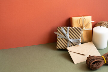 Gift box and wrapping roll, envelope, candle on khaki table. red wall background. anniversary, birthday, christmas, greeting concept
