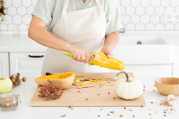 Woman hands peeling a butternut pumpkin in modern white kitchen. Homemade autumn pumpkin soup...